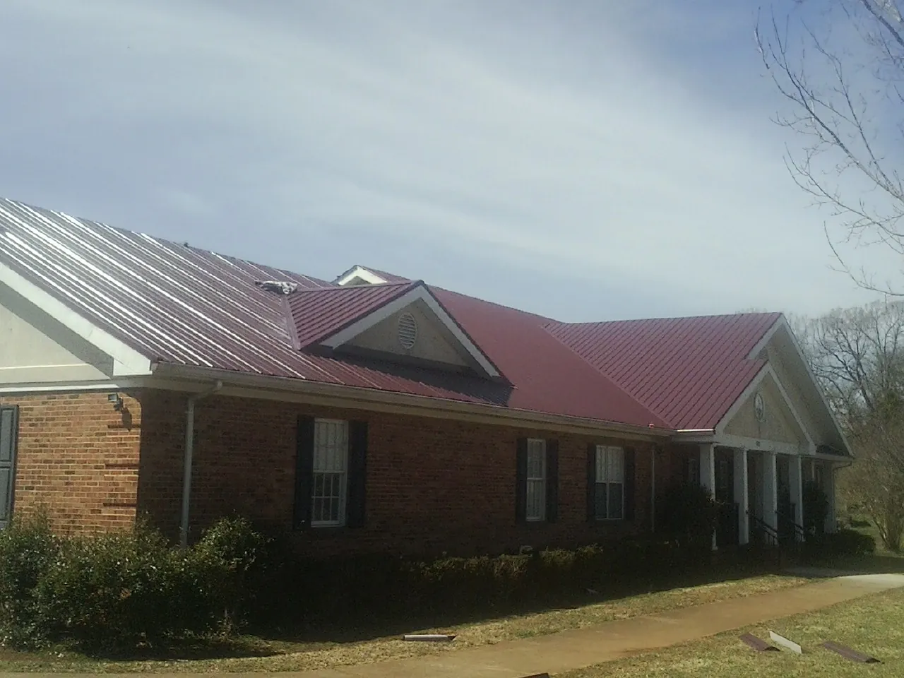 Red metal roof with gabled entries on a long brick building, from a Hail Damage Roof Repair job in Harleysville