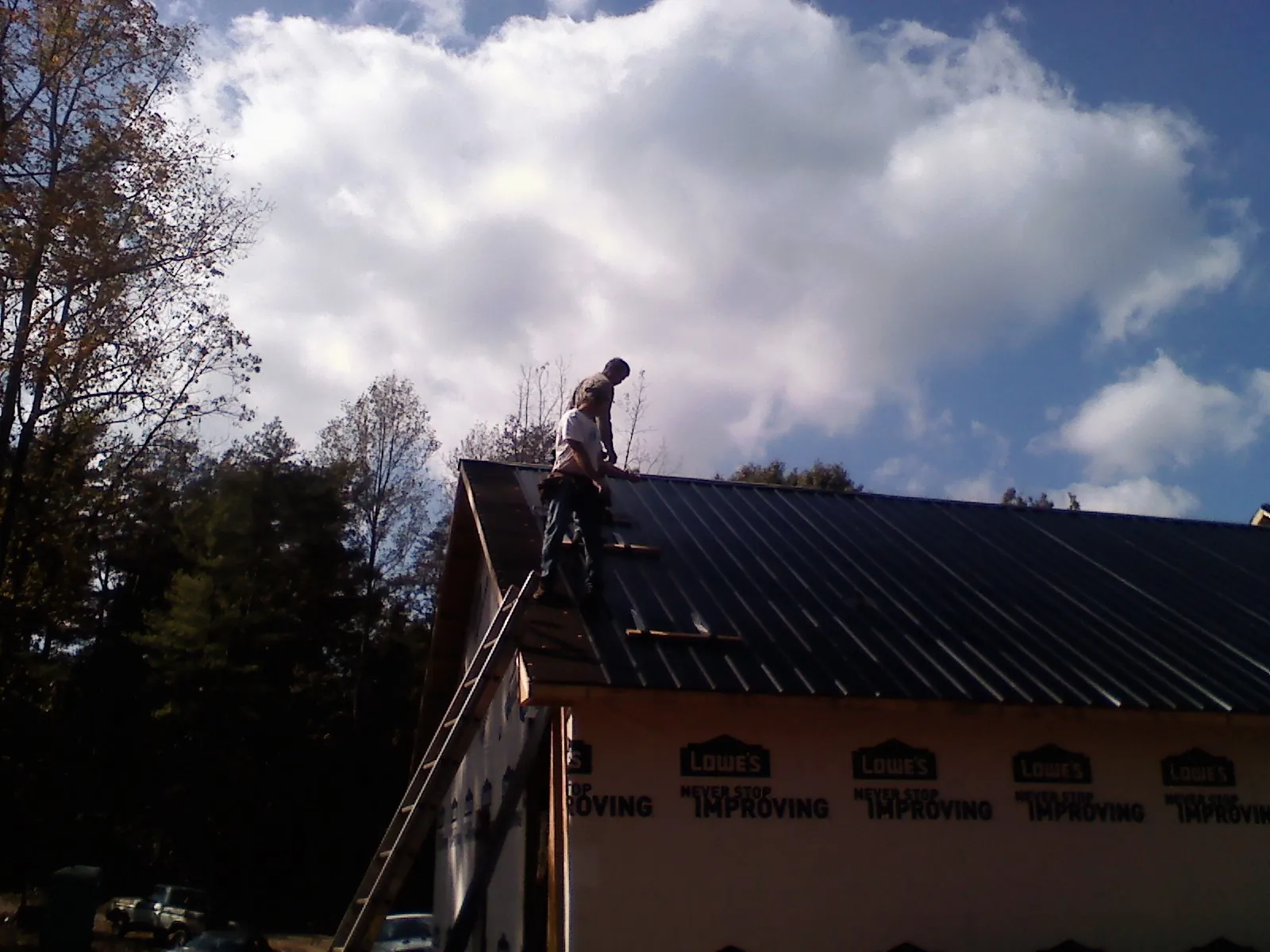 Roofer fastening dark metal panels high against a cloudy sky in Harleysville