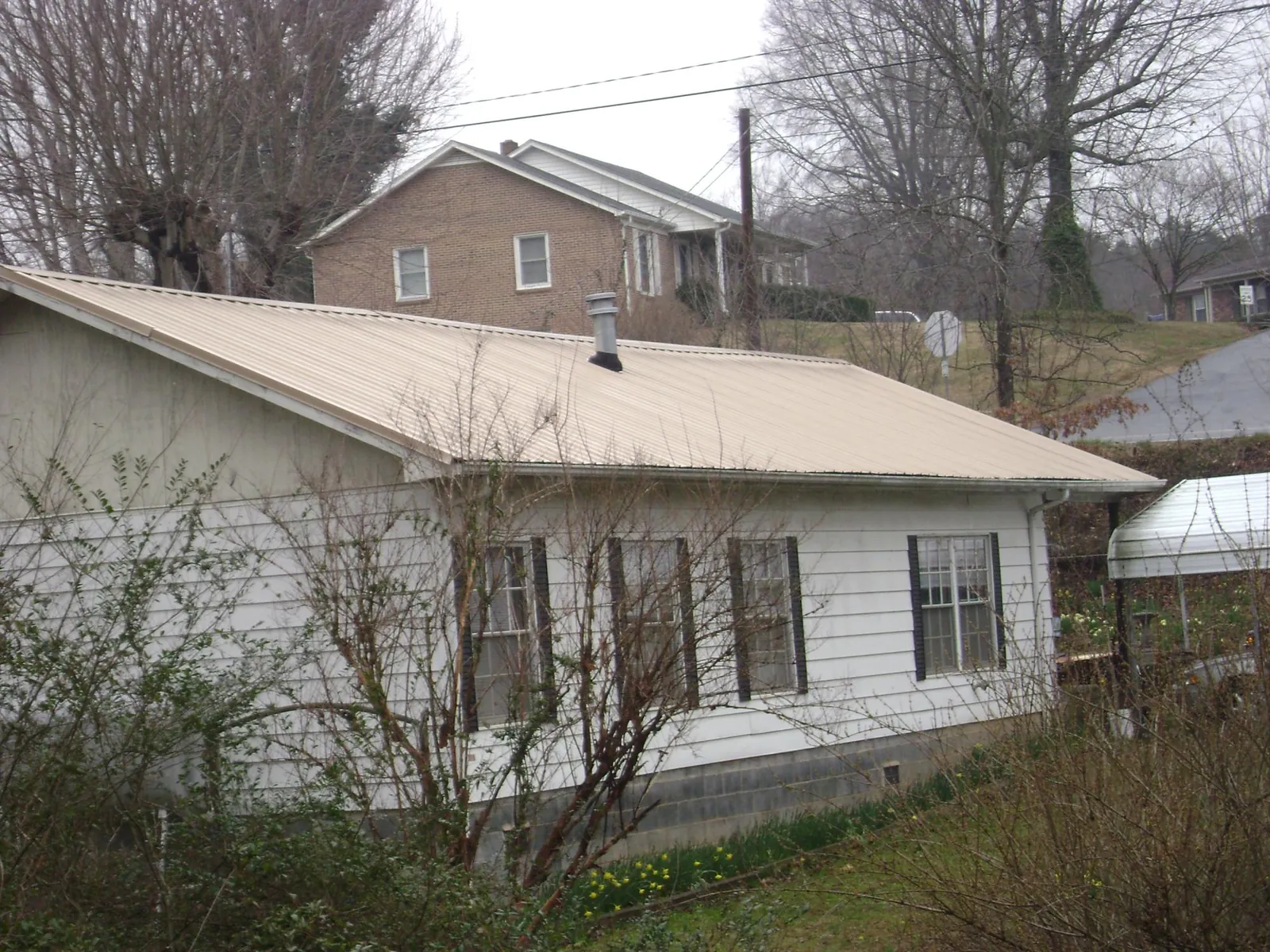 Tan metal roof on a white sided house set into a hillside — Commercial Roofing by Roofing Brothers in Harleysville